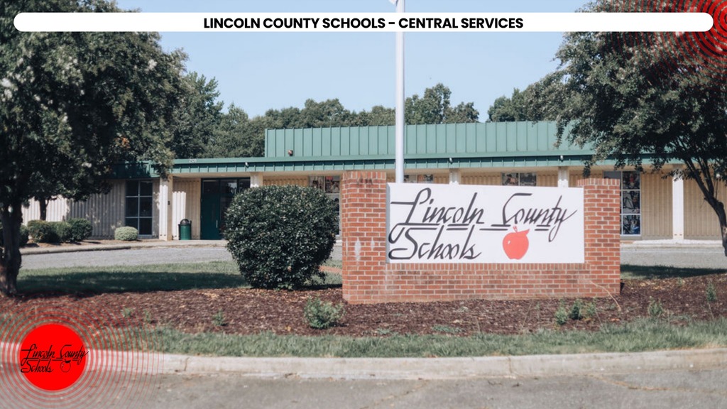 Green sign with "Lincoln County Schools" in white letters, red apple icon, and bushes in front of building.