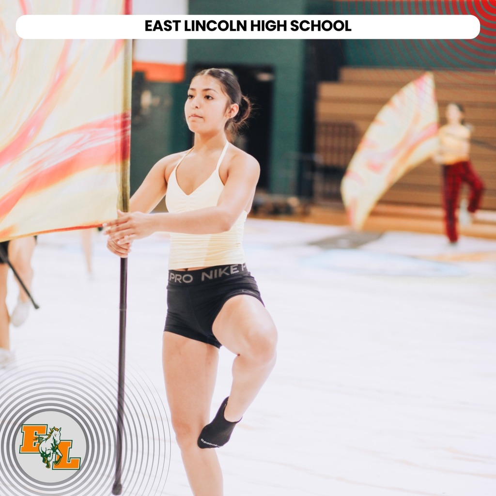 A woman at East Lincoln High School, holding a pole and flag, runs with other people in a gym.