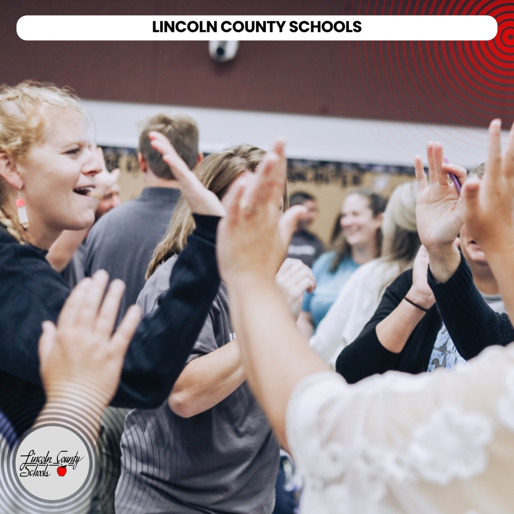 Group of adults smiling and raising their hands in a classroom with "Lincoln County Schools" text.