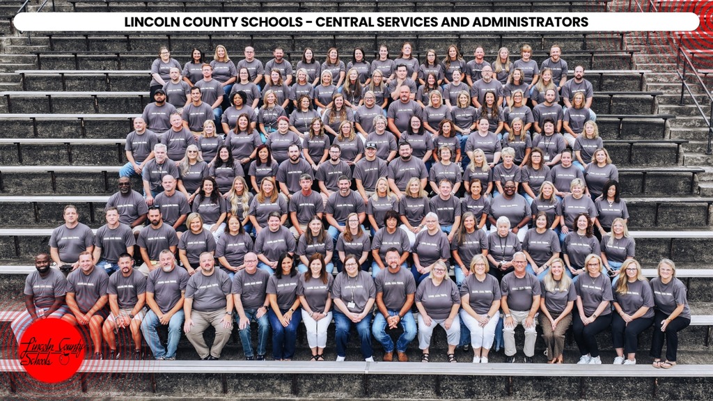 A group of people in gray shirts poses on stadium bleachers. A red circle is at the bottom left.