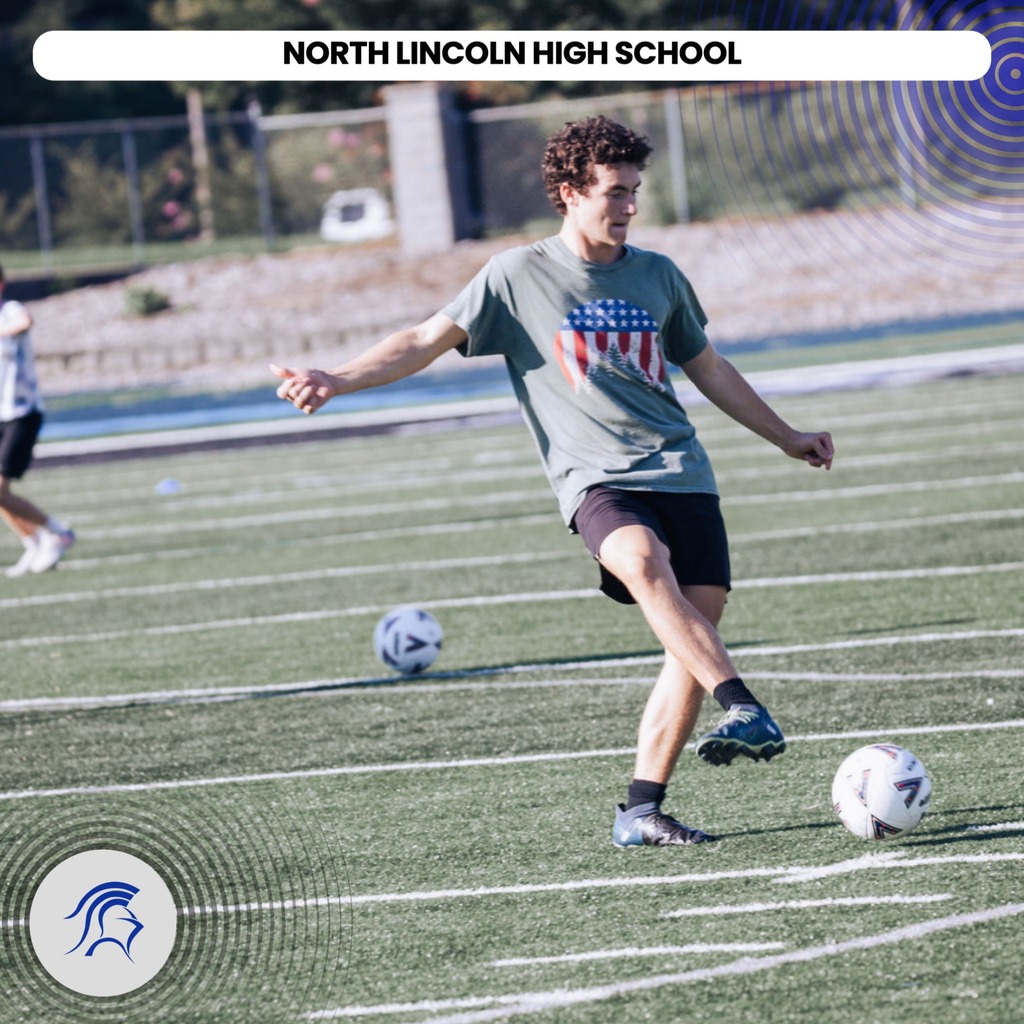 A young person in a gray tee and black shorts kicks a soccer ball on a field.