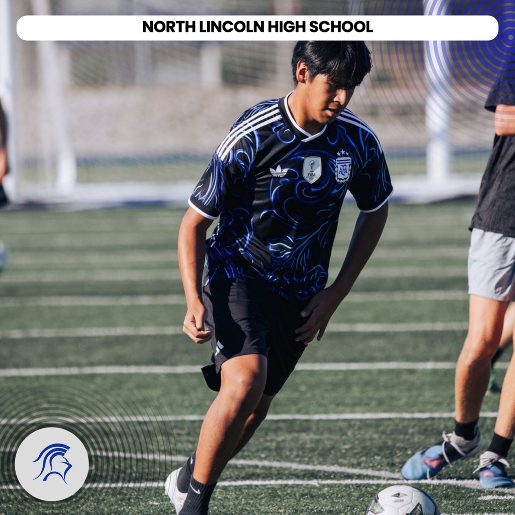 A soccer player runs on a field. He wears a blue jersey and black shorts. A white soccer ball is nearby.