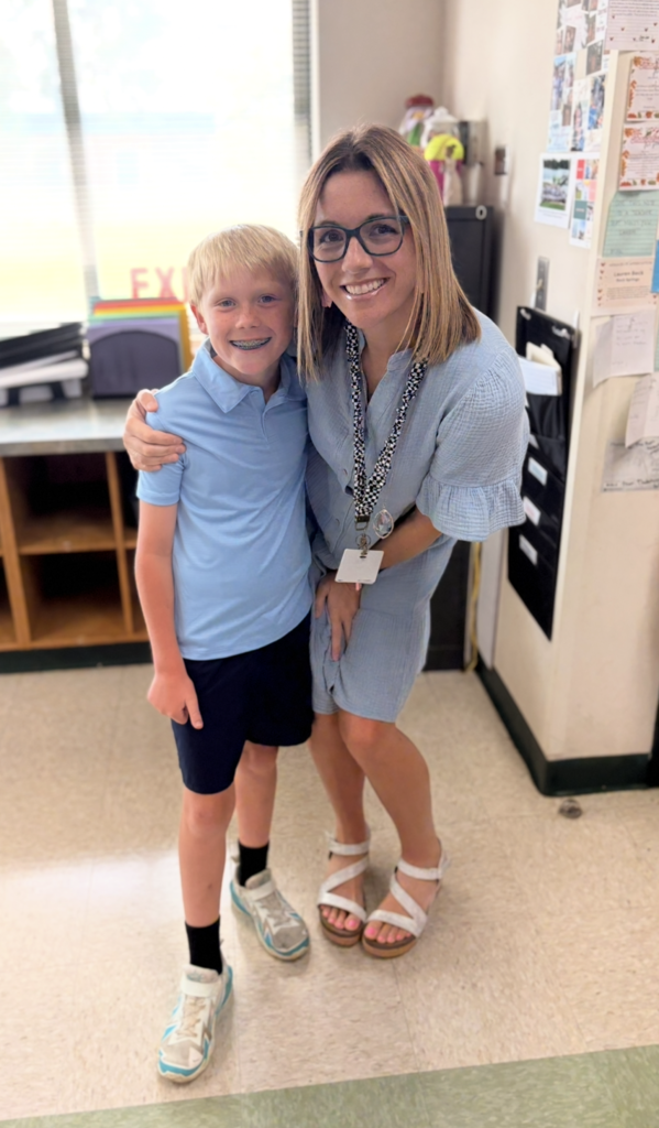 A young boy and an adult woman in a classroom. The woman has an ID on a lanyard.