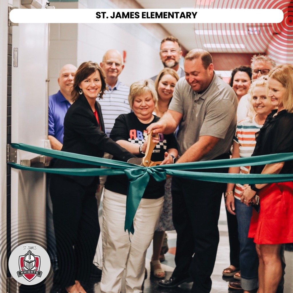 Group of adults at a ribbon cutting event, with two people cutting a green ribbon.