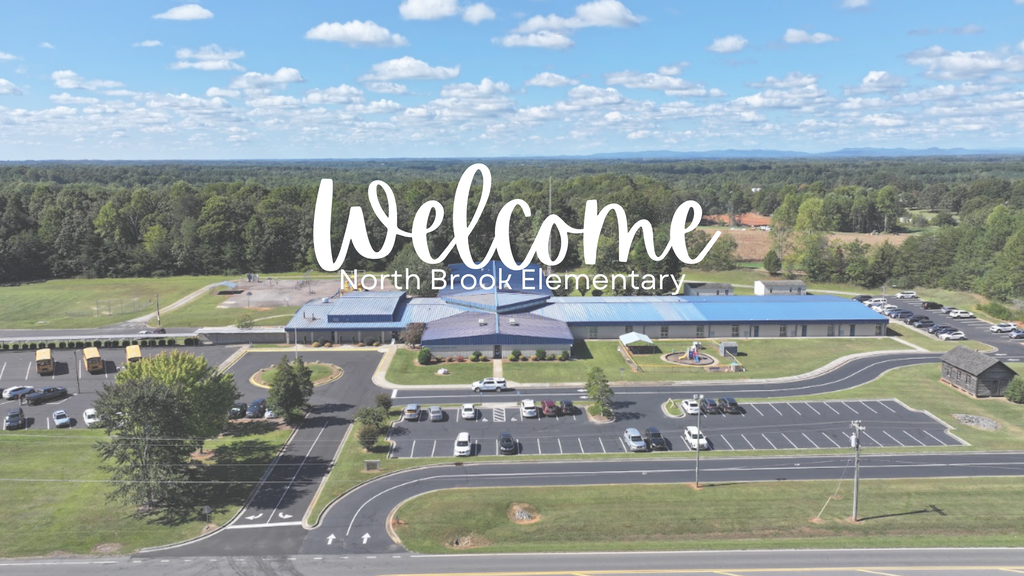 Overhead view of a school, "Welcome" text above, surrounded by a parking lot, trees, and a road.