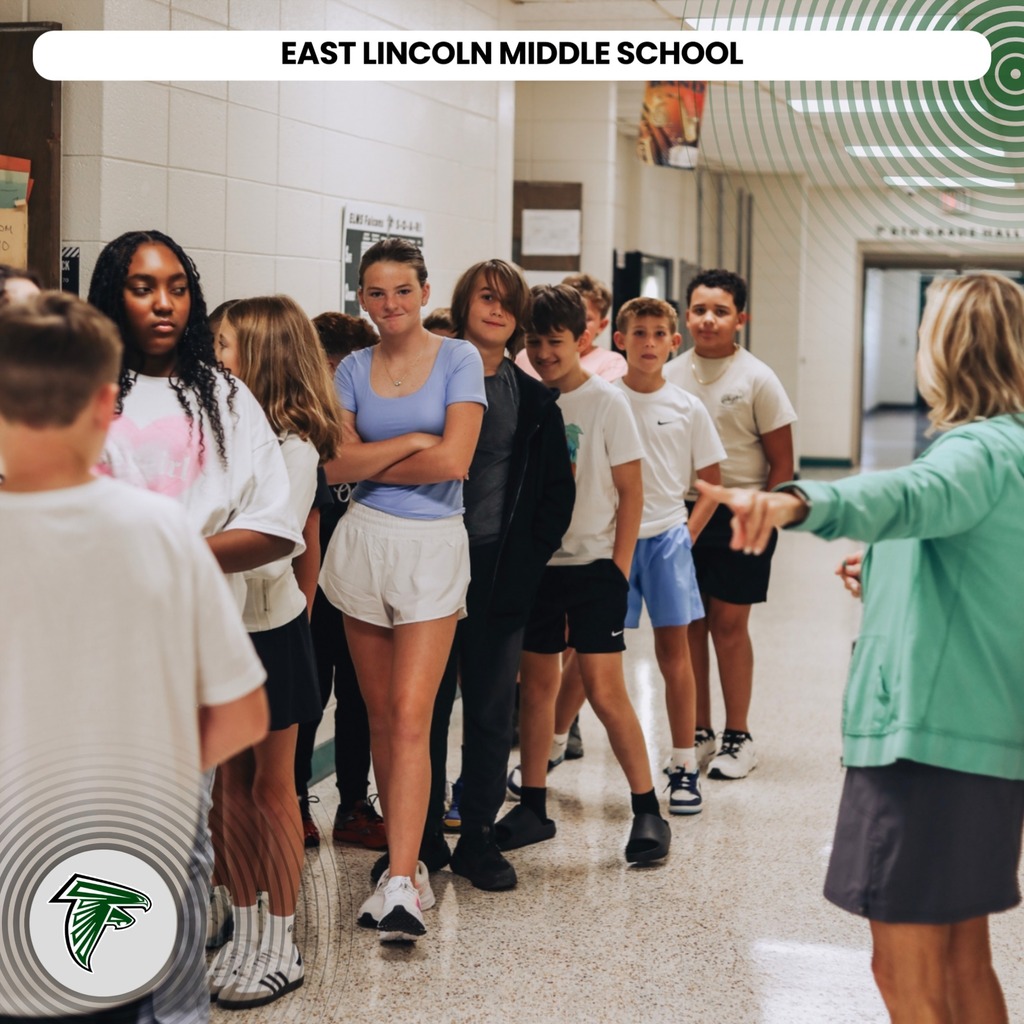 A hallway with kids. A woman speaks to students in front of a sign for East Lincoln Middle School.