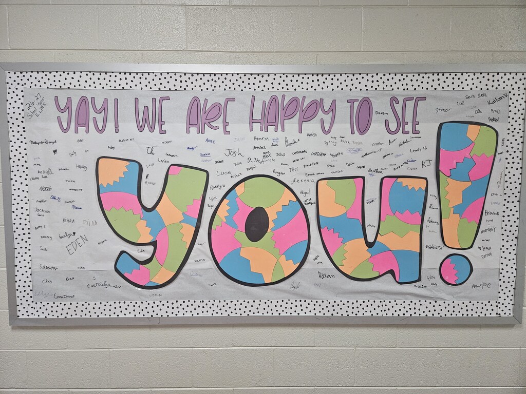 A white banner with black polka dots displays colorful, cut-out letters reading "Yay! We are happy to see you!" against a white background.