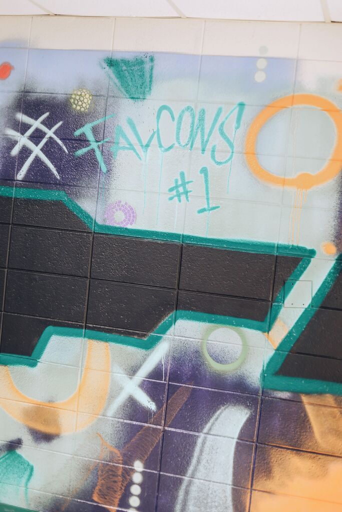 A wall with graffiti, including an arrow pointing right, "Falcons #1" in large white letters, and various other colorful spray paint.
