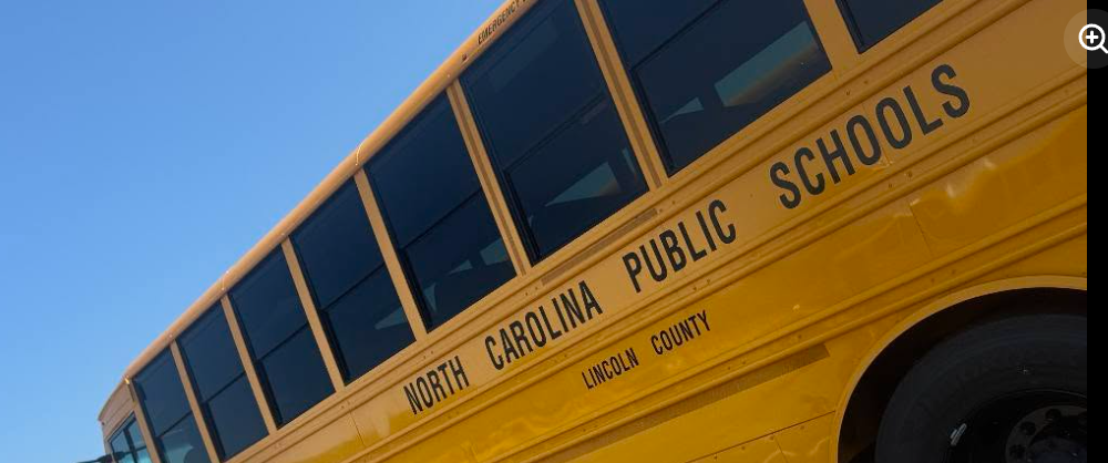 A yellow school bus from North Carolina Public Schools, with black windows, against a clear blue sky.