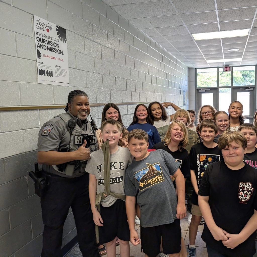 A police officer stands with several children in a school hallway, some wearing school shirts.