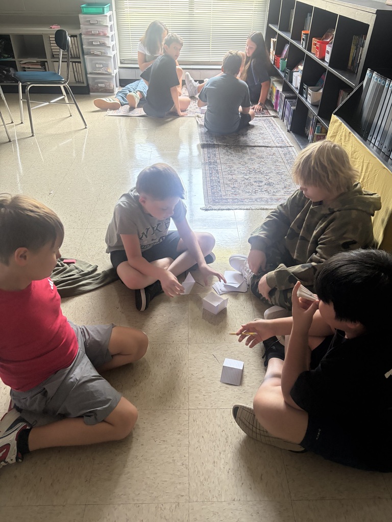 A group of children sit in a circle on the floor, engaging in a game with cubes.