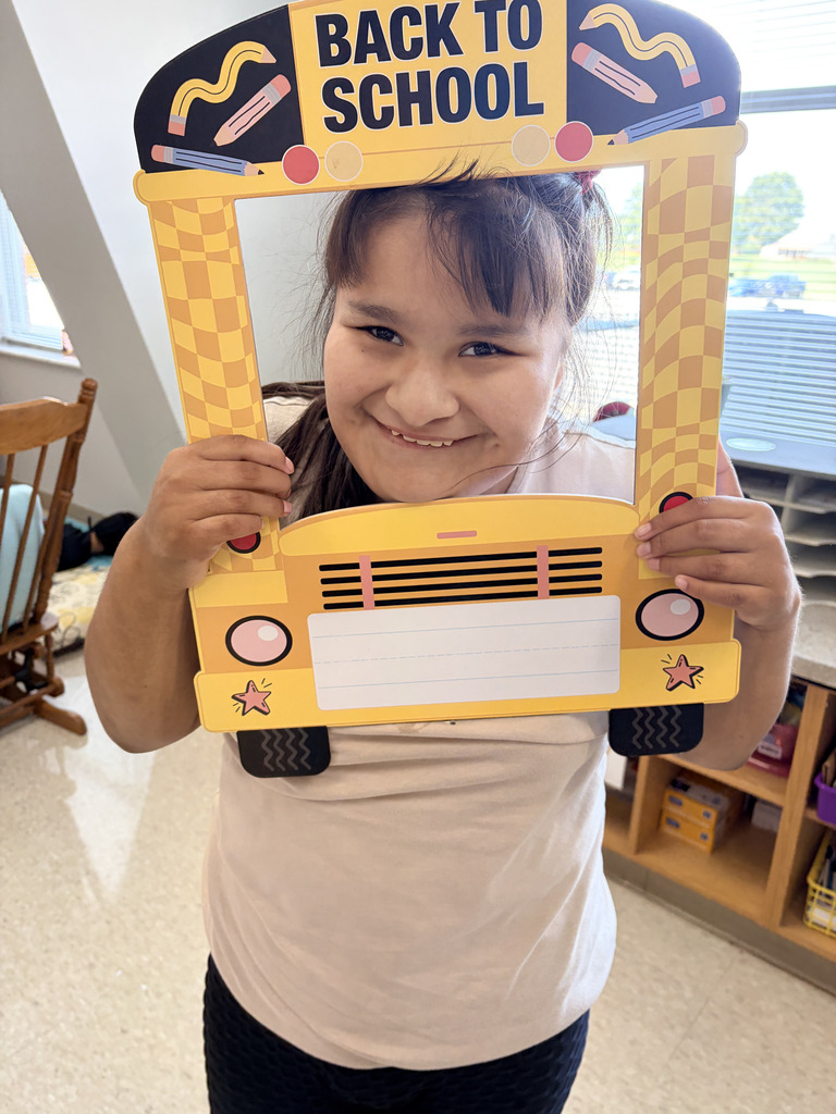 A girl holding a yellow frame shaped like a school bus with "Back to School" written on it.