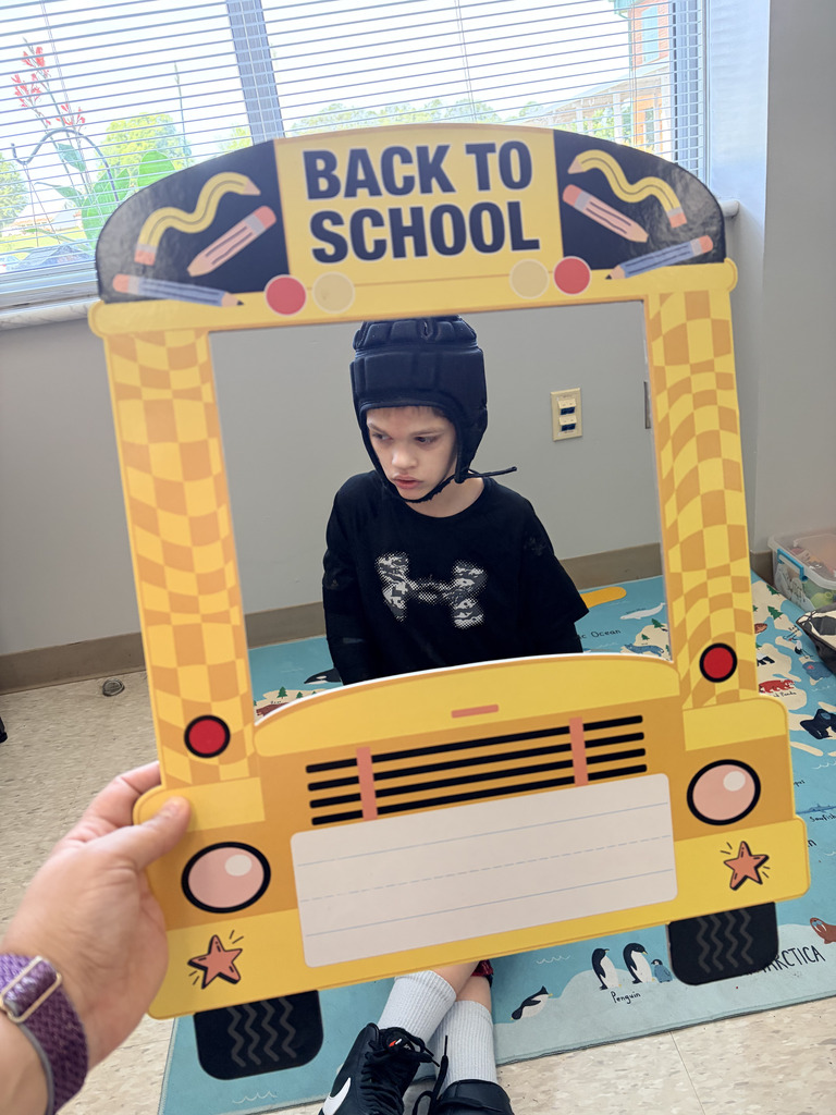 A child wearing a helmet stands inside a photo frame shaped like a school bus. The photo frame reads "Back to School."