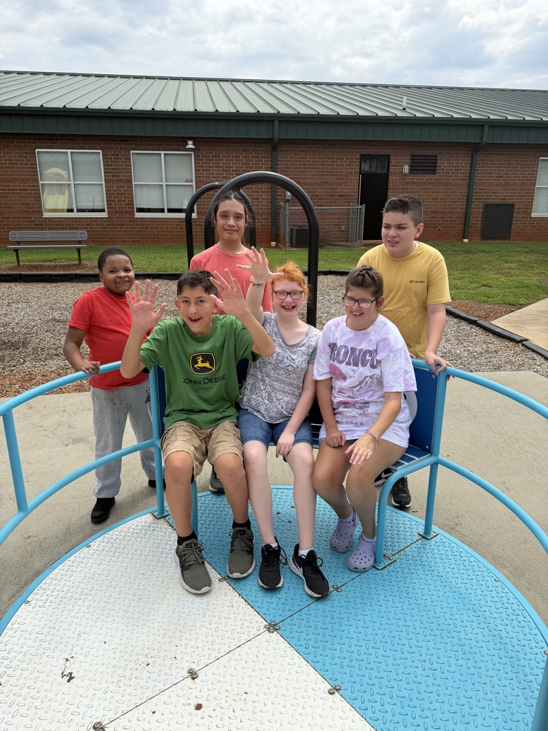 Six children on a merry-go-round. A building is behind them, with some windows and a roof.