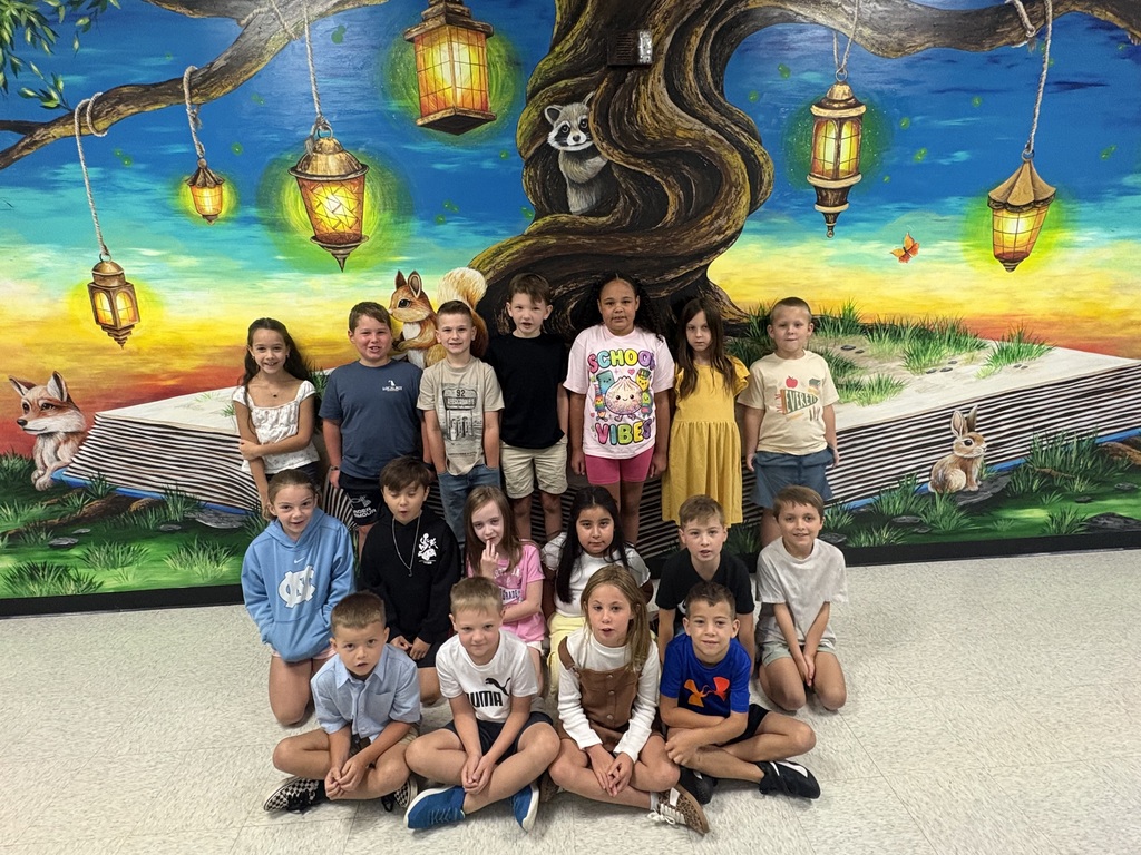Kids pose in front of a mural featuring a tree, hanging lanterns, and an open book.