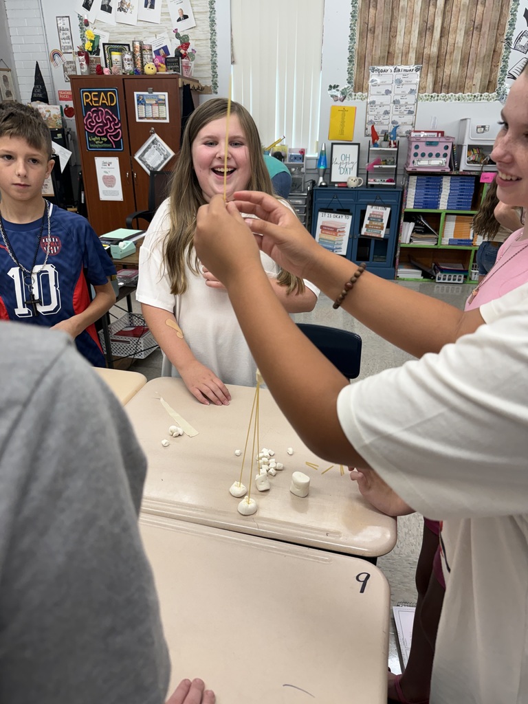 Several students work together at a table with a string of marshmallows and toothpicks.
