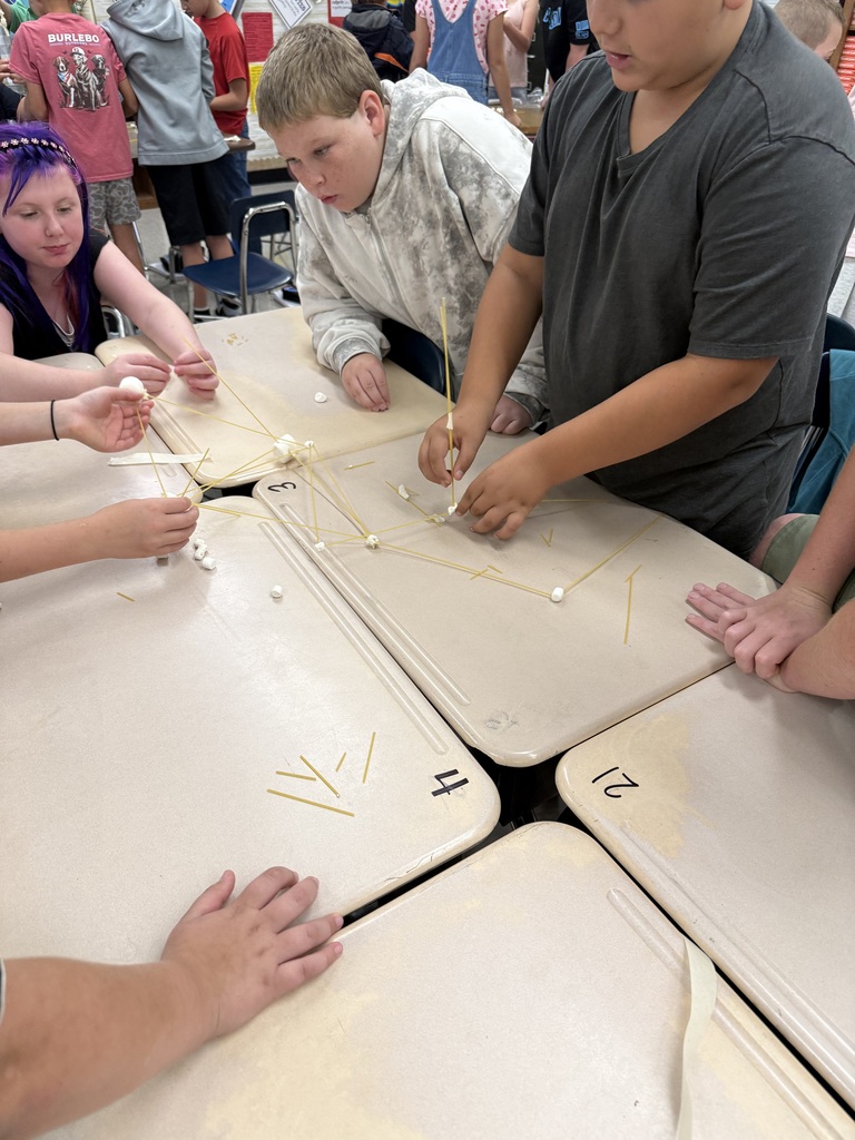 A group of students work together on a table, using sticks and beads to create structures.