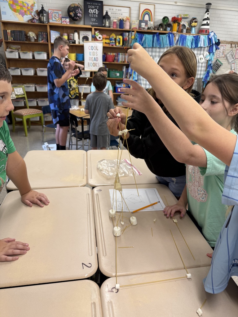 Several children working on a classroom project with a stick and string structure on a table.