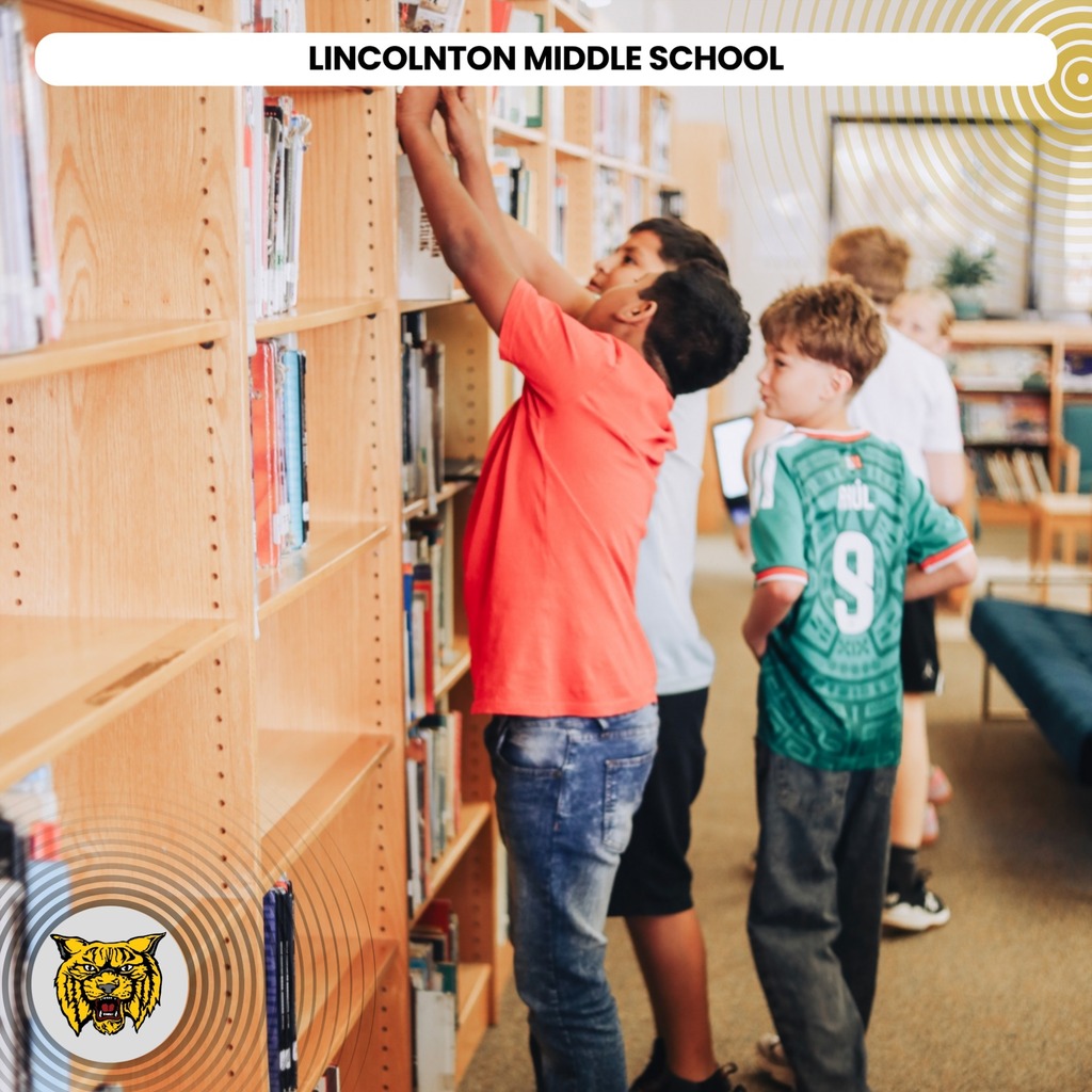 Kids in a library. One boy is reaching for books on the top shelf. Another boy is looking up.