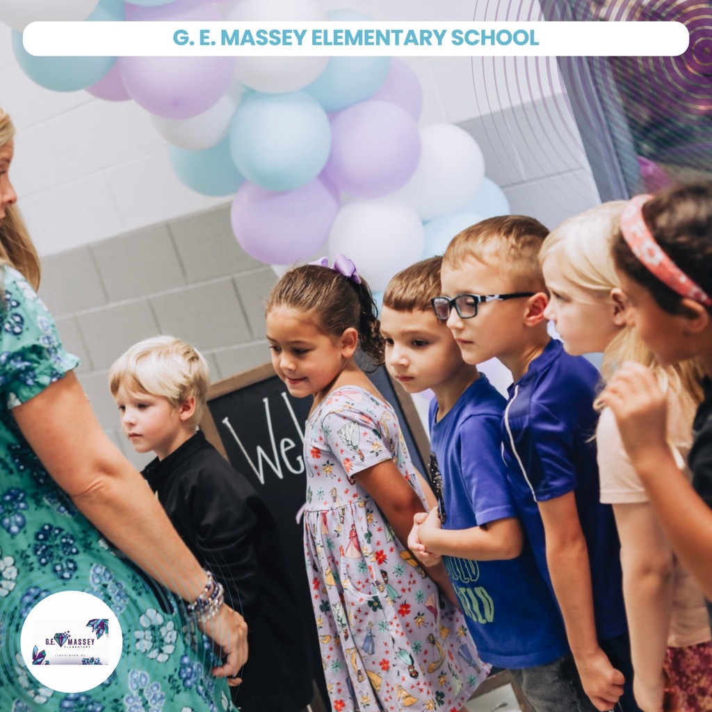 Group of children in line at a school. A teacher stands before them. Background has balloons.