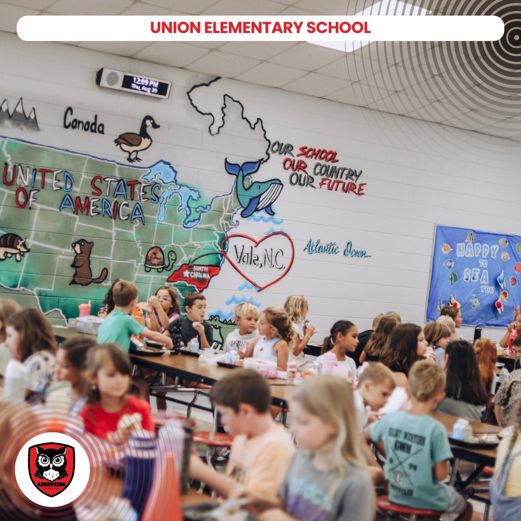 Classroom with students seated at tables. A U.S. map mural with "United States of America" and other text.