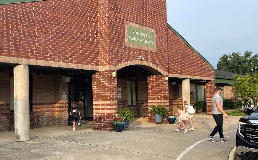 A brick building with a sign reading "Rock Springs Elementary School". People are walking in front of it.