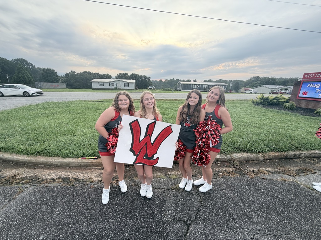 Four girls in matching red and black cheerleading uniforms hold a large white sign with the letter W.