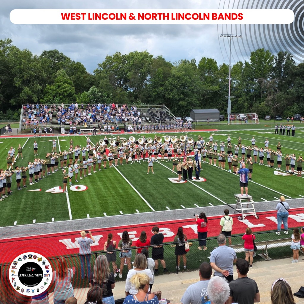 A marching band performs on a football field with spectators in stands. Trees and a gray sky are in the background.