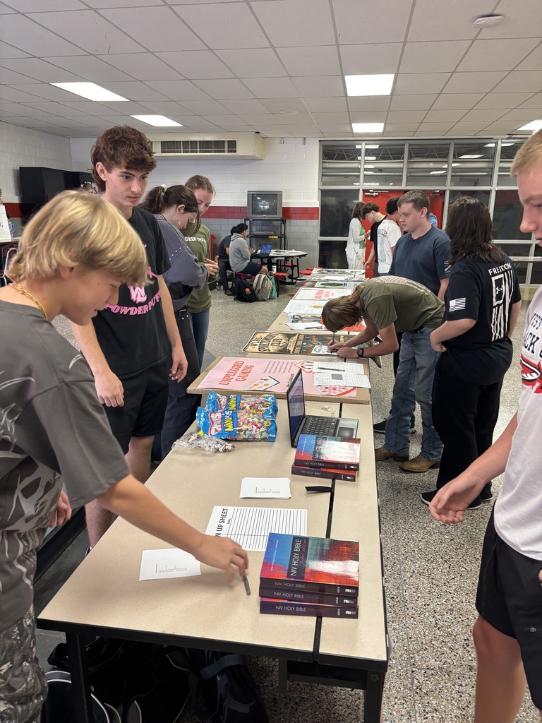 Group of students gathered around tables in a room, signing books and browsing at a book event.