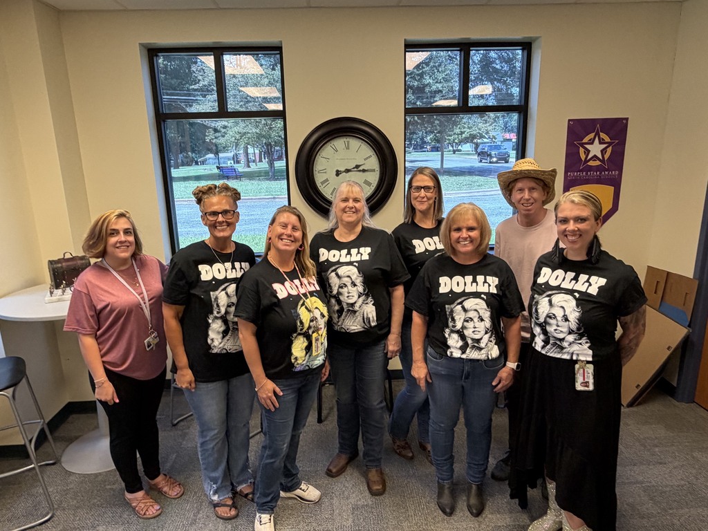 A group of women in matching black shirts with the word "DOLLY" are posing for a photo.