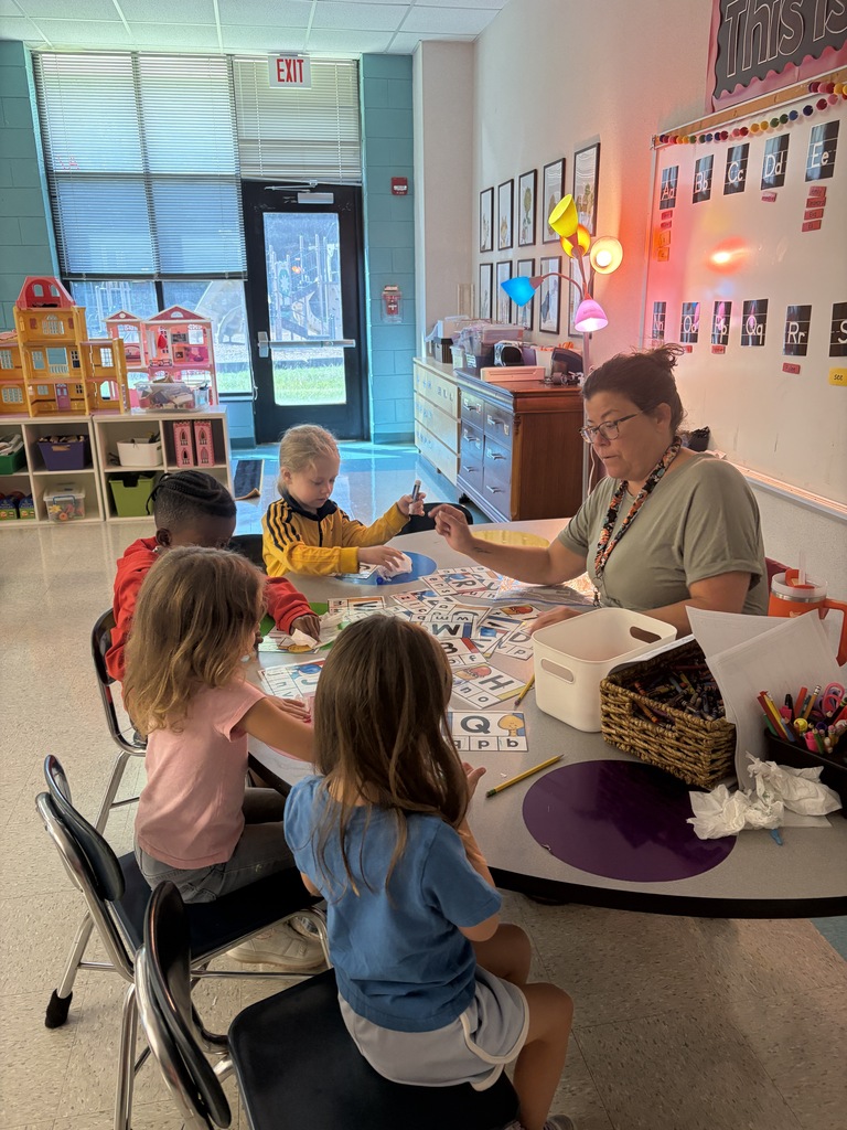 Several young children and an adult woman sit around a table, engaging in an activity.