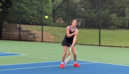 A person in black playing tennis on a blue court, hitting a ball in the air.