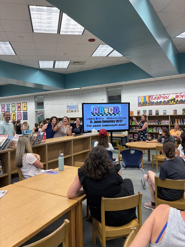 Library with tables and chairs. A large screen at the front of the room displays a title.