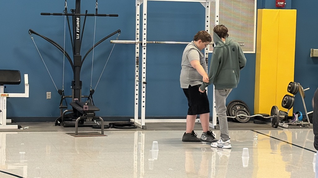 Two people are standing in a gym with a blue wall and yellow equipment behind them.