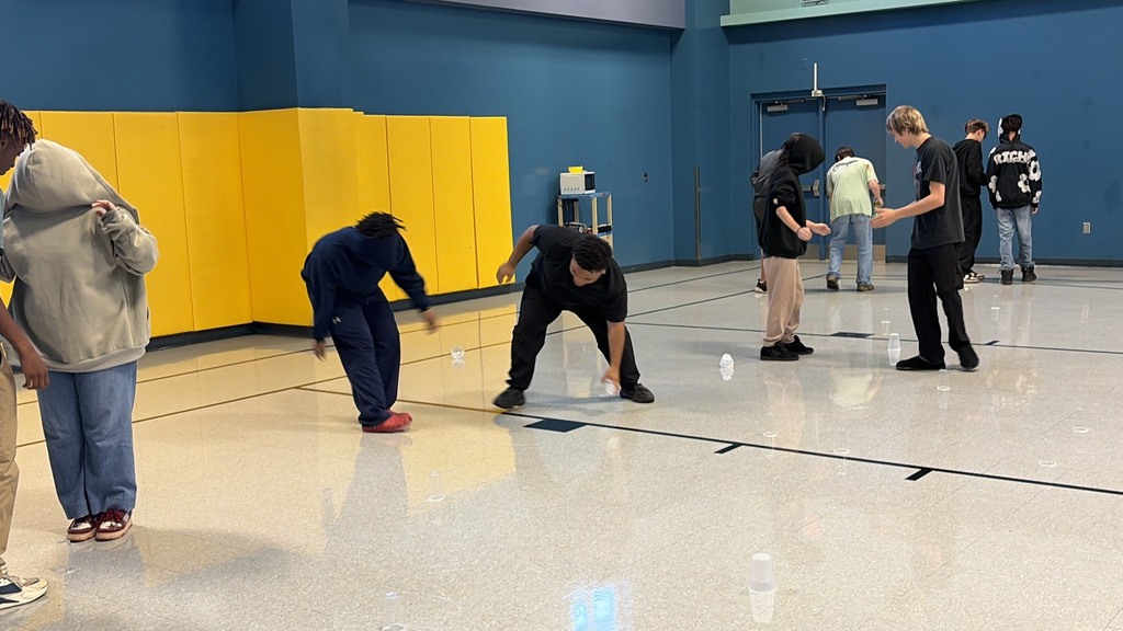Several people in a room with blue and yellow walls, standing and bending down, playing a game.