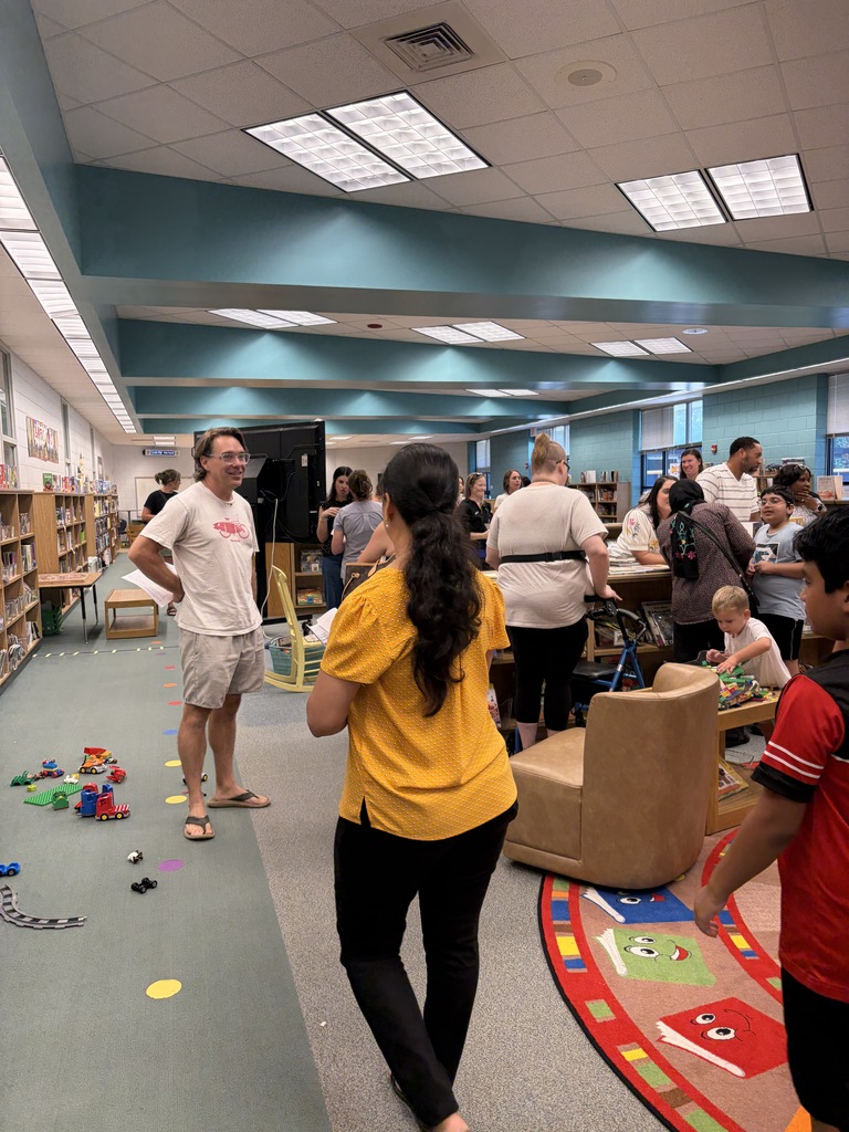A room with people, one standing in sandals, one with a yellow shirt, a wheelchair, toys, and chairs.