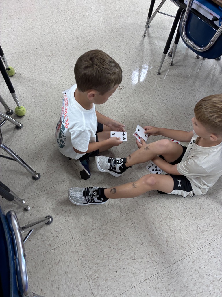 Two boys sitting on the floor playing a card game. One holds a card, the other holds two.