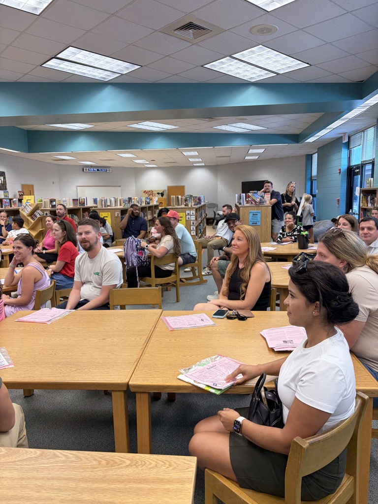 Group of people sitting at tables in a library with books and papers on the tables.