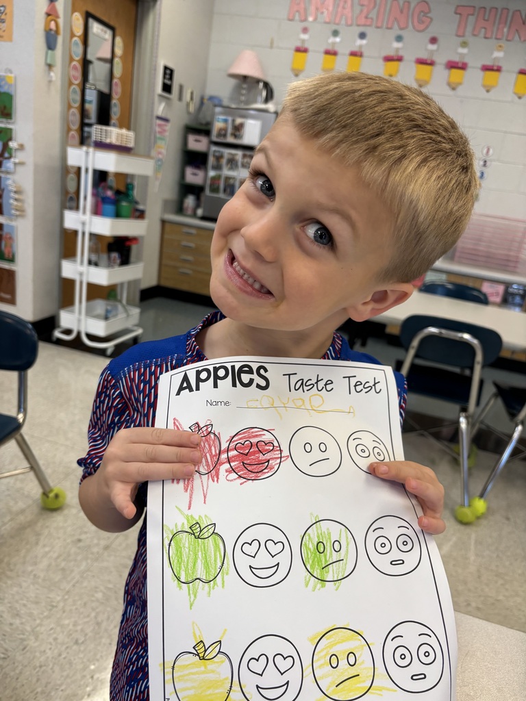 Student holding a paper showing how he rated red, green, and yellow apples.