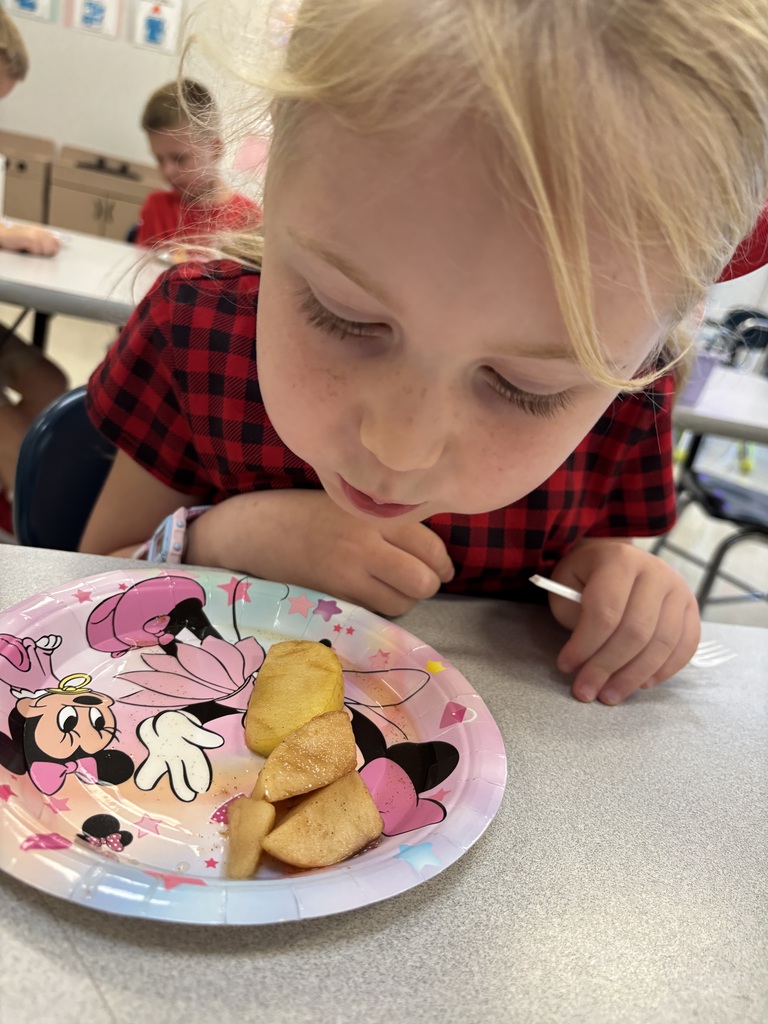 A young child eats food from a plate with a Minnie Mouse design. The table has a white surface.