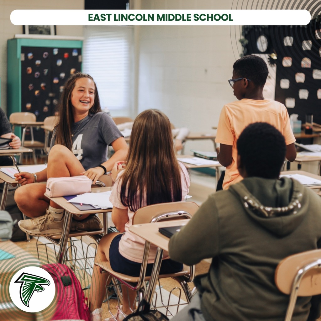 A classroom with students seated around desks, one smiling, another with a backpack, and a school logo.