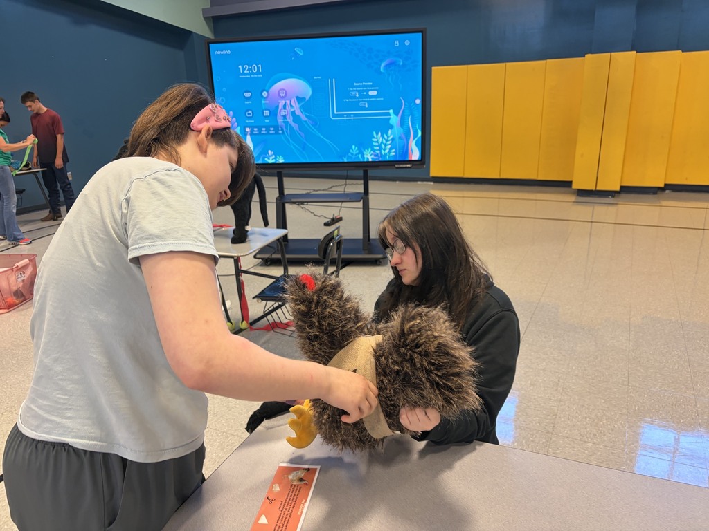 Two people are in a room with a large screen and yellow walls. One holds a stuffed animal.