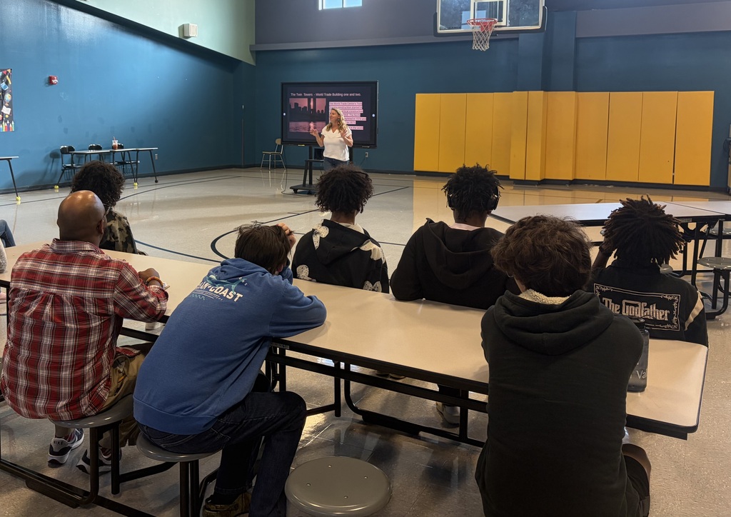 A table of students sits and listens to a 9/11 presentation from a teacher