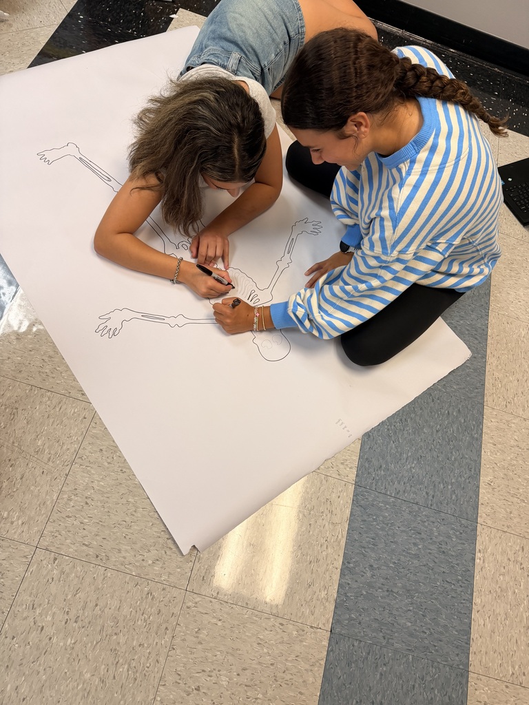 Two individuals are working together on a large white paper with a drawing on a tiled floor.