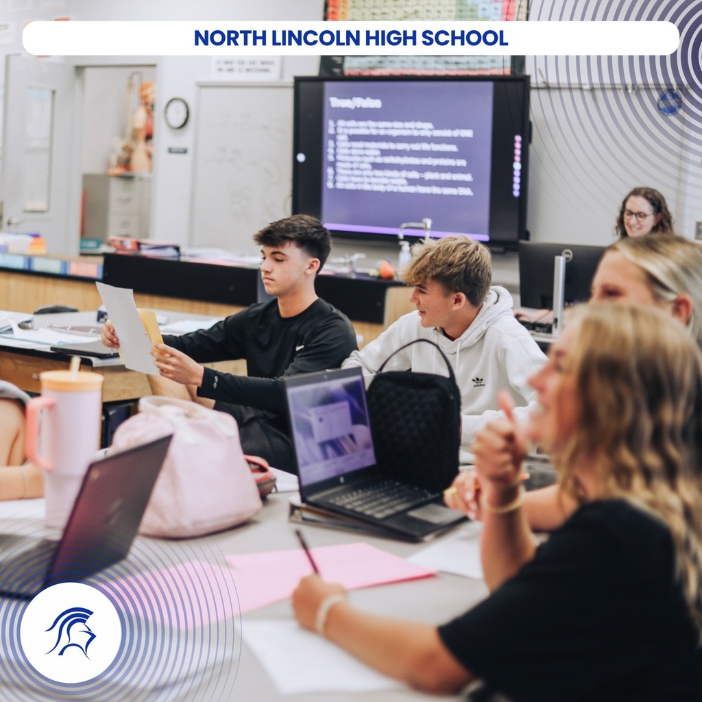 High school students at North Lincoln High School, seated around a table with laptops, engage in a classroom setting.