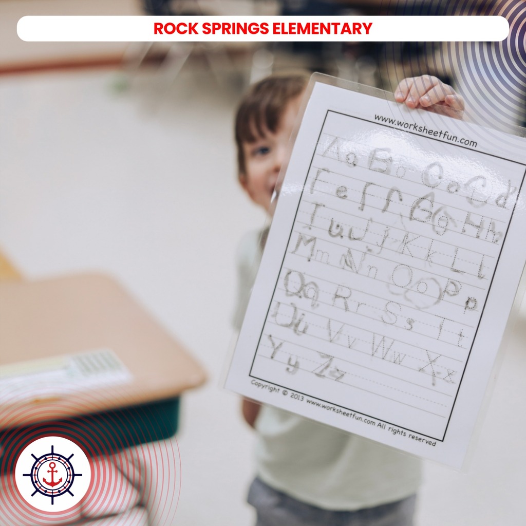 Child in a classroom holding a worksheet for Rock Springs Elementary, with alphabet lines on the paper.