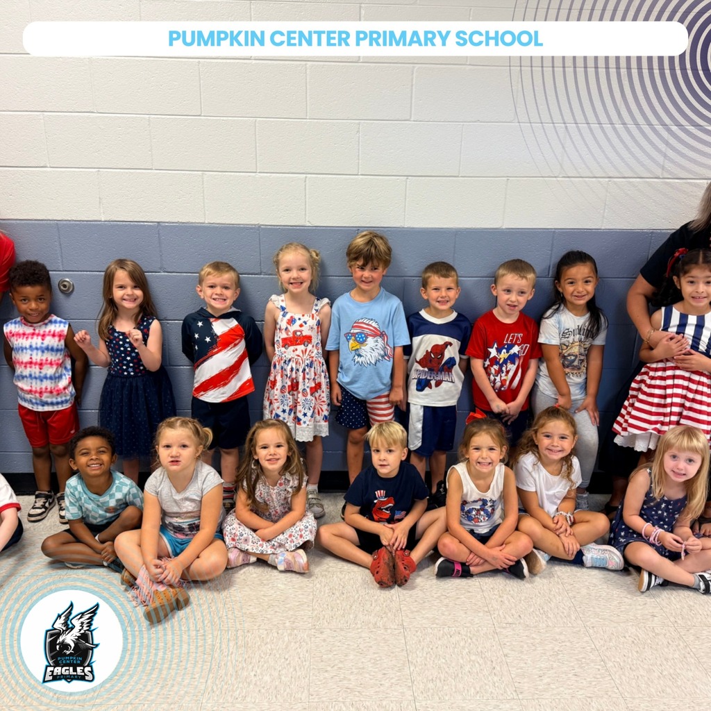 A group of children in colorful outfits sit or stand near a wall with a school name.