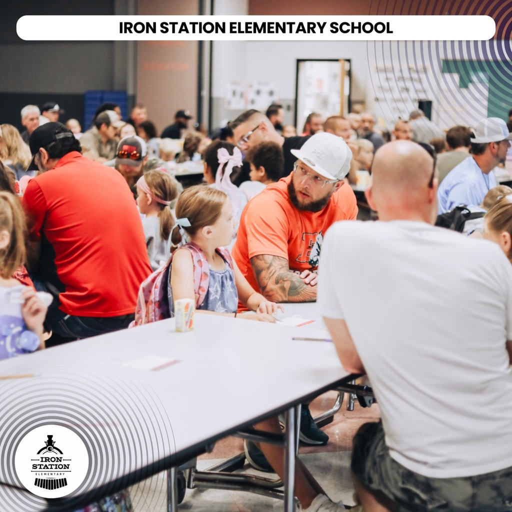 Group of adults and children at tables inside a room. Text reads "IRON STATION ELEMENTARY SCHOOL" in the top center.