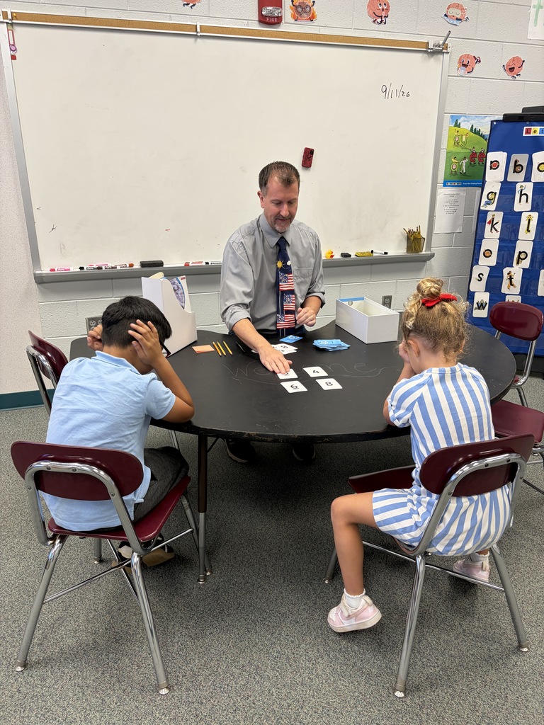 A man and two children sitting at a round table, the man has cards and they are looking at them.