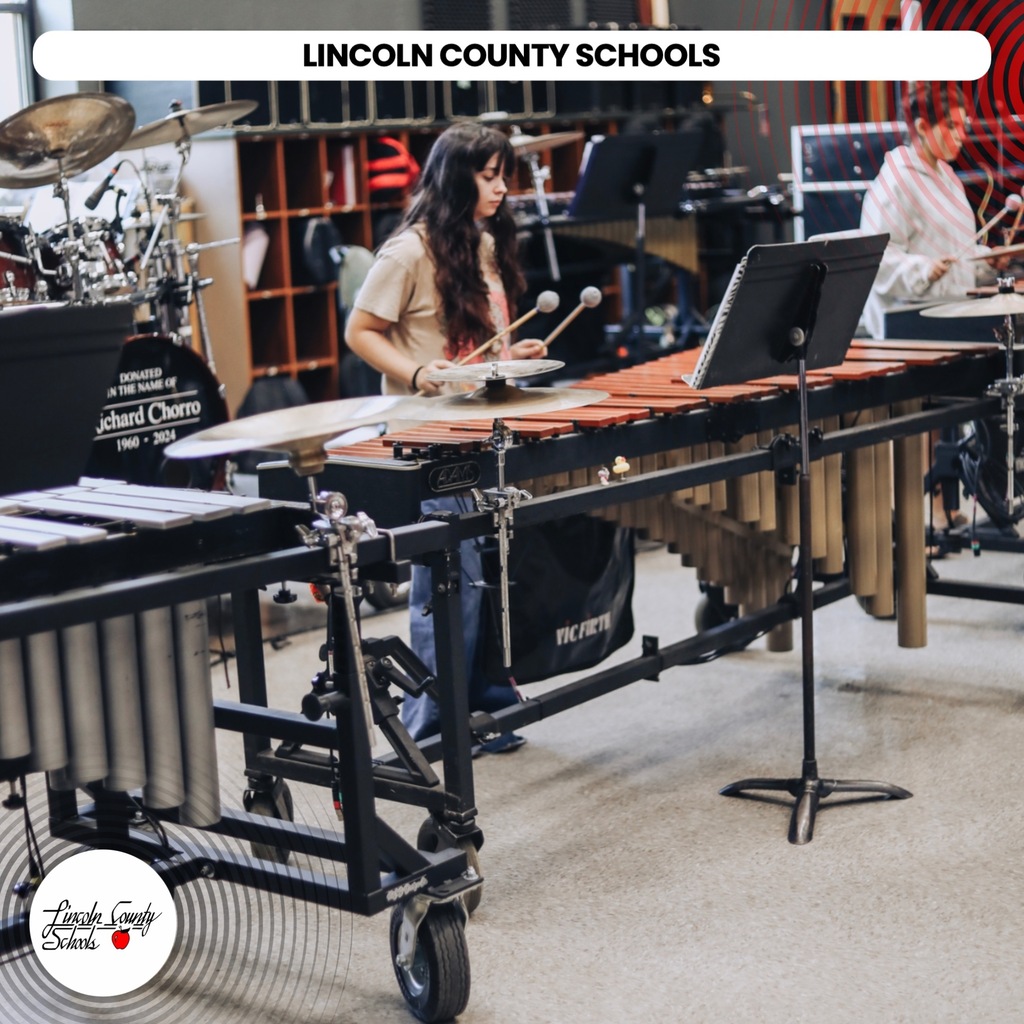 A student plays a xylophone with mallets in a music room. Other musical instruments are visible.